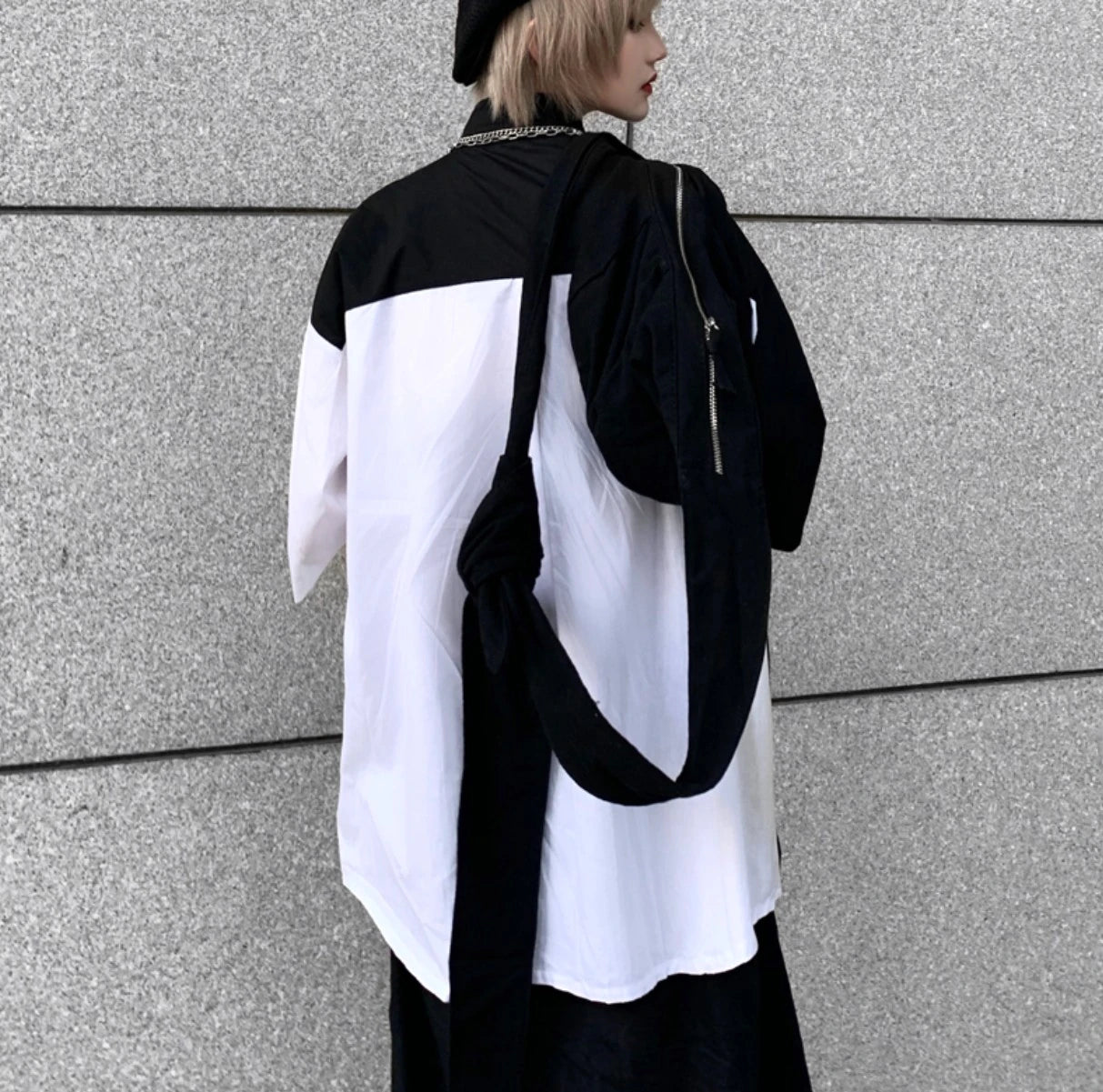 白と黒のバイカラーシャツを着たモデルの後ろ姿(上半身)。黒いバッグを肩にかけている。