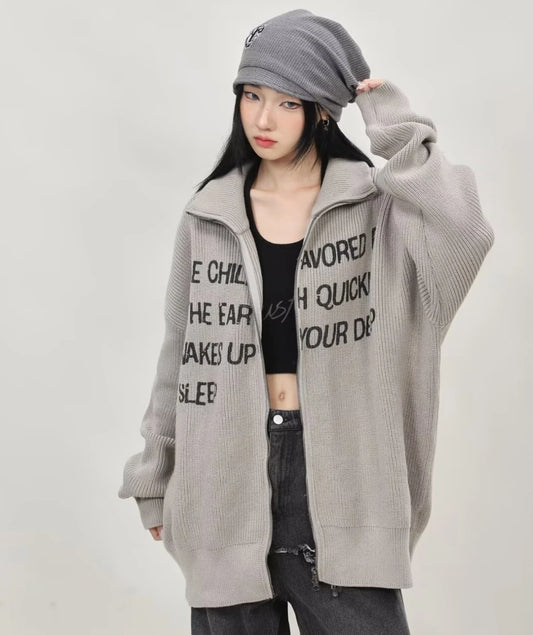 グレーの英字メッセージジップニットカーディガンを前開きで羽織り、ビーニーとワイドデニムを合わせたレディースコーデの正面全身