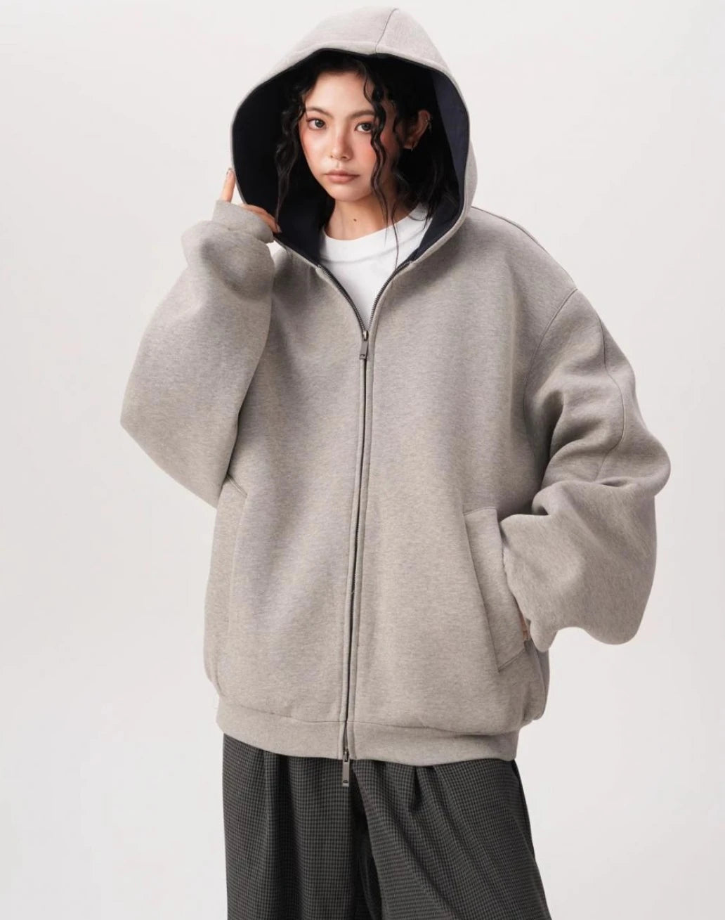 フードを深くかぶったモデルがグレーのオーバーサイズジップパーカーを前ファスナー閉めで着用している写真