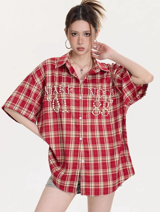 胸ポケットにパール装飾が並んだレッドチェック柄オーバーサイズシャツのフロントスタイリングカット。ボタンを留めた着こなしが見える。
