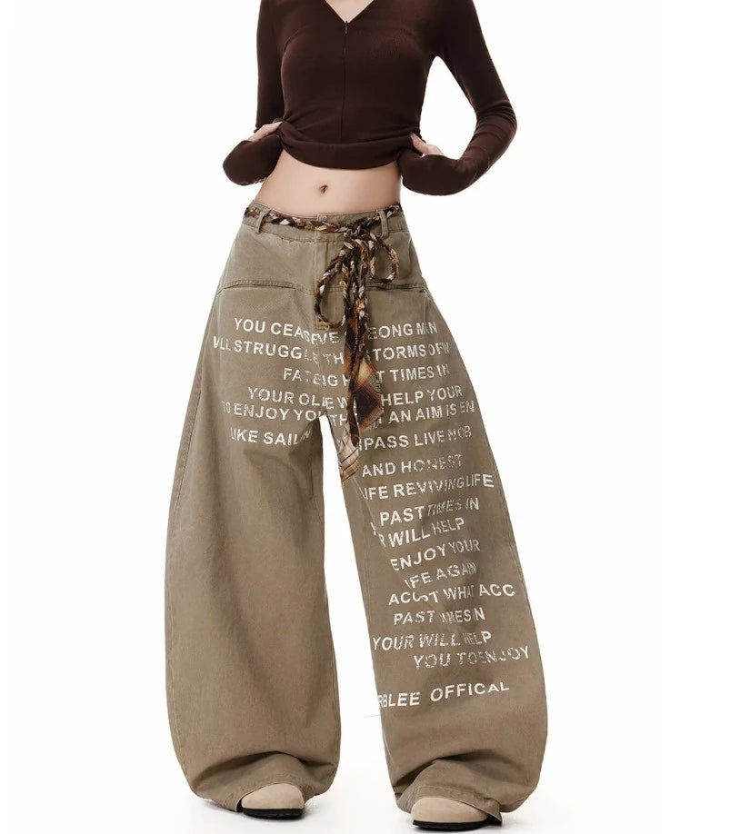 ベージュの極太バギーパンツを着用した全身正面。白の英字プリントと、共布のベルトが垂れたデザイン。茶色のクロップドトップスとコーディネート。