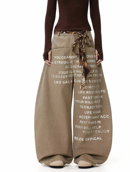 ベージュのバギーパンツを着用した全身正面。パンツにプリントされた英字の文章がよく見える構図。
