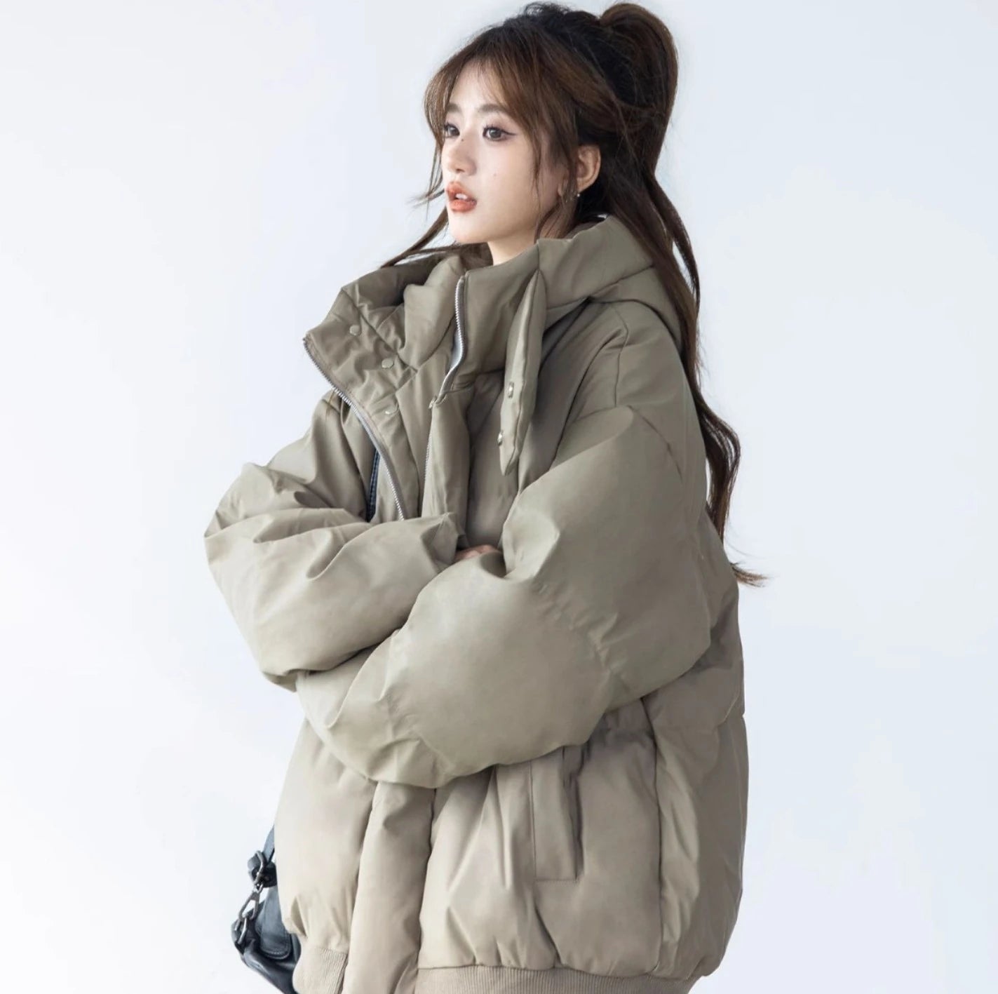 ベージュ/カーキのショートダウンジャケットを着た女性モデルのポートレート。腕を組み、ハイネックの襟元を強調している。