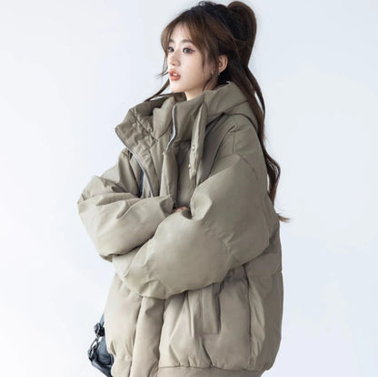 ベージュ/カーキのショートダウンジャケットを着た女性モデルのポートレート。腕を組み、ハイネックの襟元を強調している。