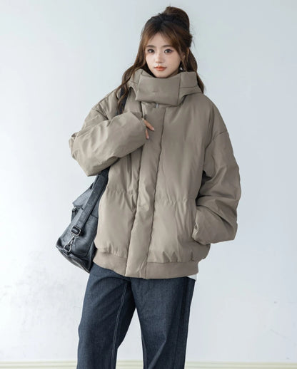 ベージュ/カーキのショートダウンと濃色ジーンズを着用した女性モデルの全身像。黒のショルダーバッグを肩に掛けている。