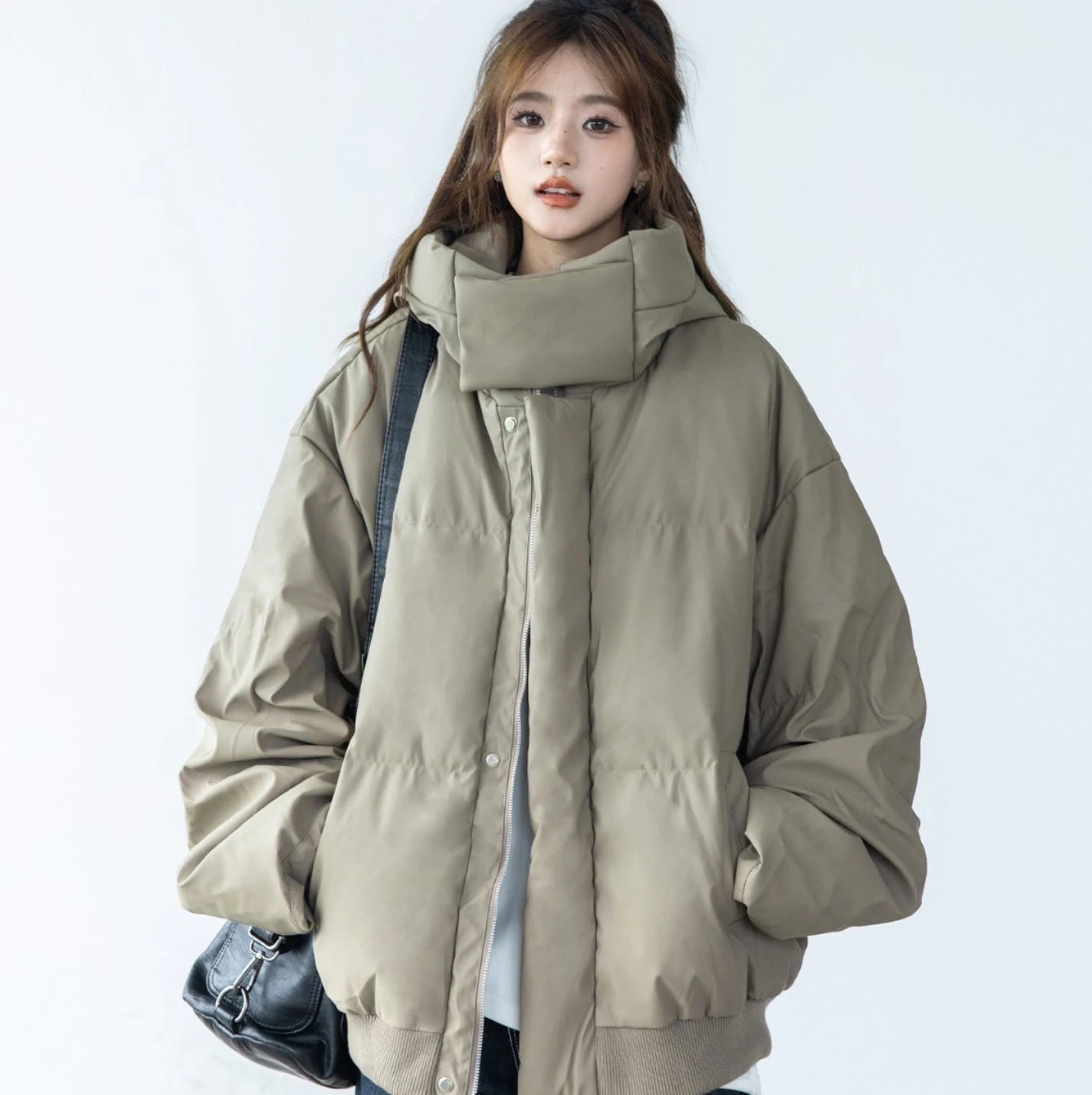 ベージュ/カーキのショートダウンを着たモデルのバストアップ。ハイネックの襟元を立てており、黒いショルダーバッグを着用。