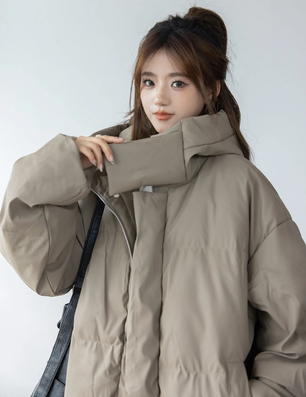 ベージュ/カーキのショートダウンを着たモデルのクローズアップ。ハイネックの襟元に手を添えているポーズ。