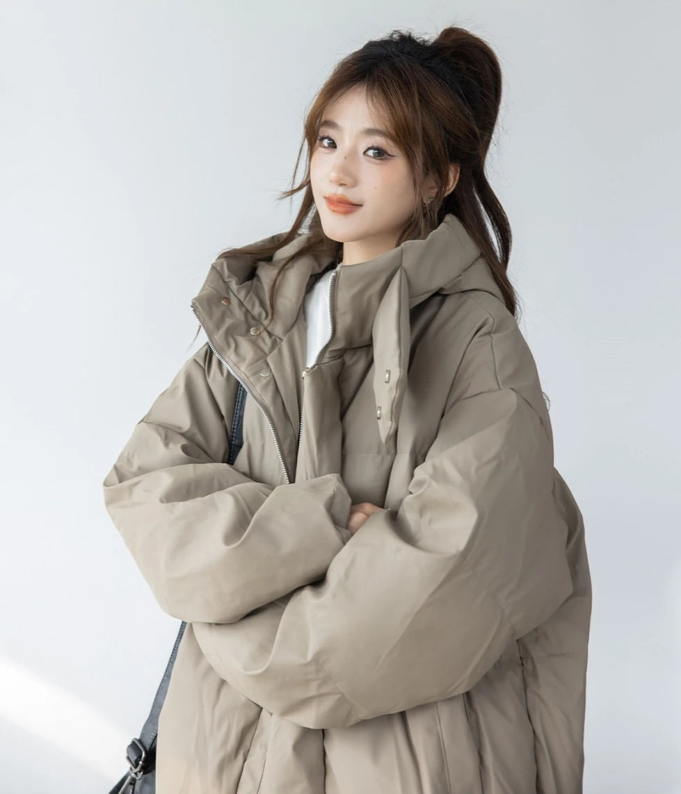 ベージュ/カーキのショートダウンを着て、笑顔で正面を向く女性モデルのバストアップ。髪はポニーテールにまとめている。