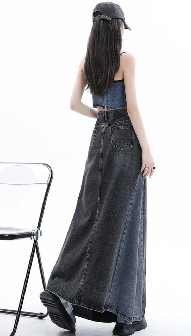 黒のロングデニムスカートを着たモデルの後ろ姿。透明な椅子の横を通り過ぎるポーズ。