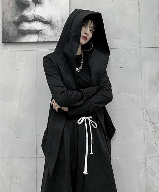 黒の変形フード付きアウターを着たモデル。フードを被り、腕組みをして立つ。