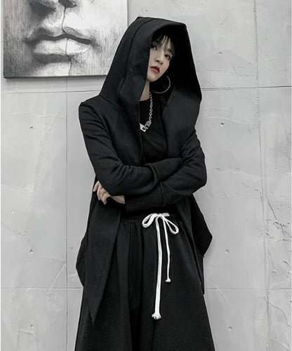 黒の変形フード付きアウターを着たモデル。フードを被り、腕組みをして立つ。
