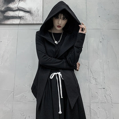 黒の変形フード付きアウターを着たモデル。フードを深く被り、首元のネックレスを見せるポーズ。