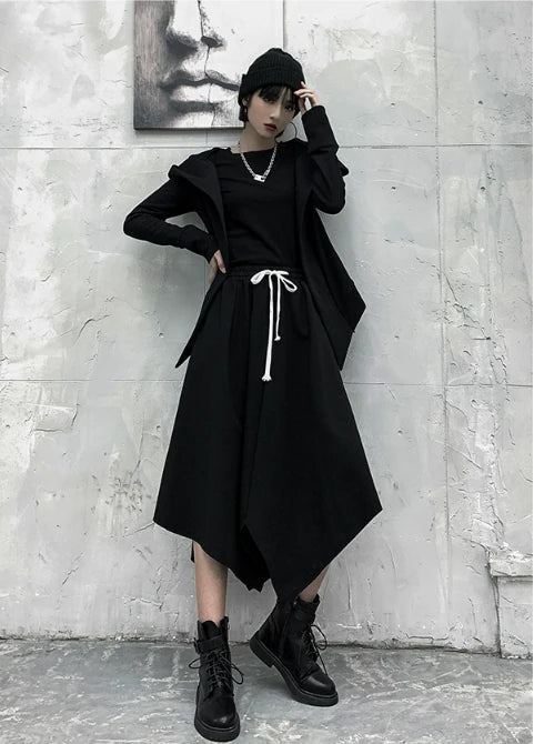 黒の変形フード付きアウターを着たモデルの全身。フードを下ろし、片手を頭に添えたポーズ。