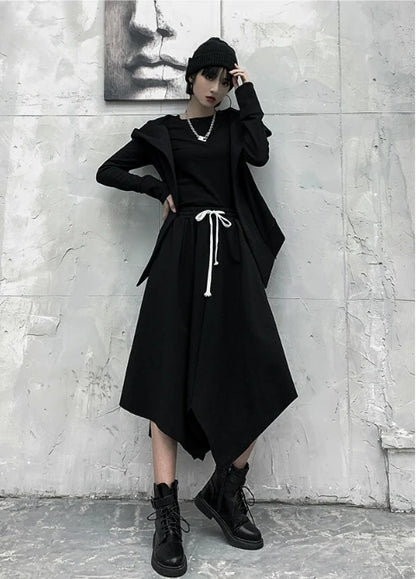 黒の変形フード付きアウターを着たモデルの全身。フードを下ろし、片手を頭に添えたポーズ。