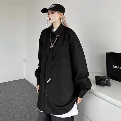 黒のオーバーサイズシャツを着用し、横を向いたポーズ。襟元のメタルチェーンとネクタイ風デザインが特徴的なストリートスタイル。