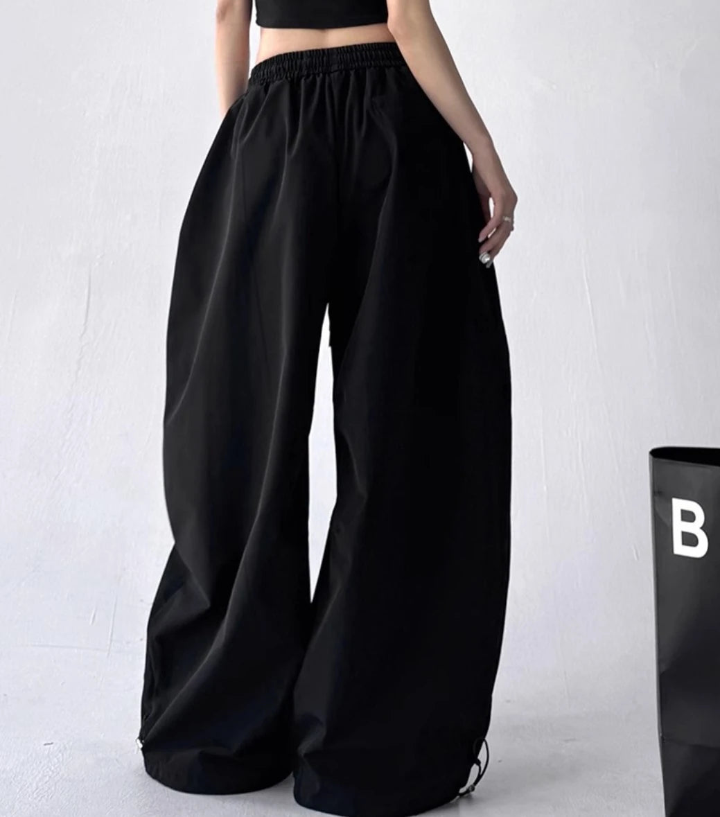 黒いパラシュートパンツを着用した後ろからの全身写真。特徴的なワイドシルエットと、裾のドローコードが確認できる。