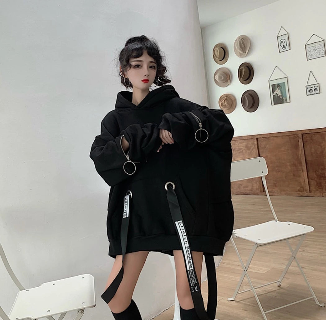 黒のオーバーサイズパーカーを着たモデル。正面で少し前傾姿勢、袖のリングジップを見せる。