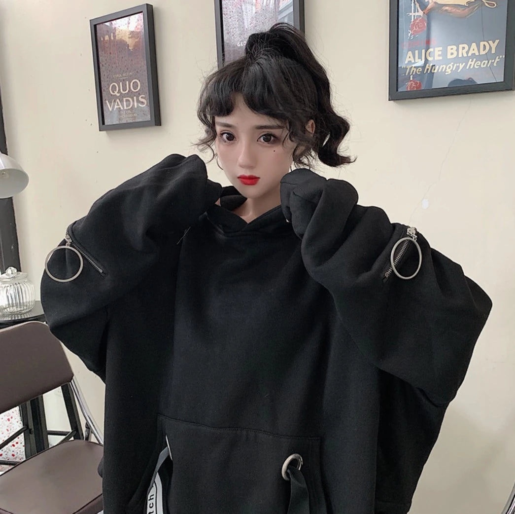 黒のオーバーサイズパーカーのバストアップ。両手でフードの襟元を持つポーズ。