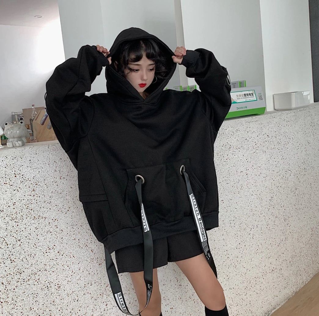 黒のオーバーサイズパーカーを着たモデル。両手でフードの縁（ふち）を持つポーズ。