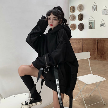 黒のオーバーサイズパーカーを着たモデル。白い椅子に片足を乗せて座るポーズ。