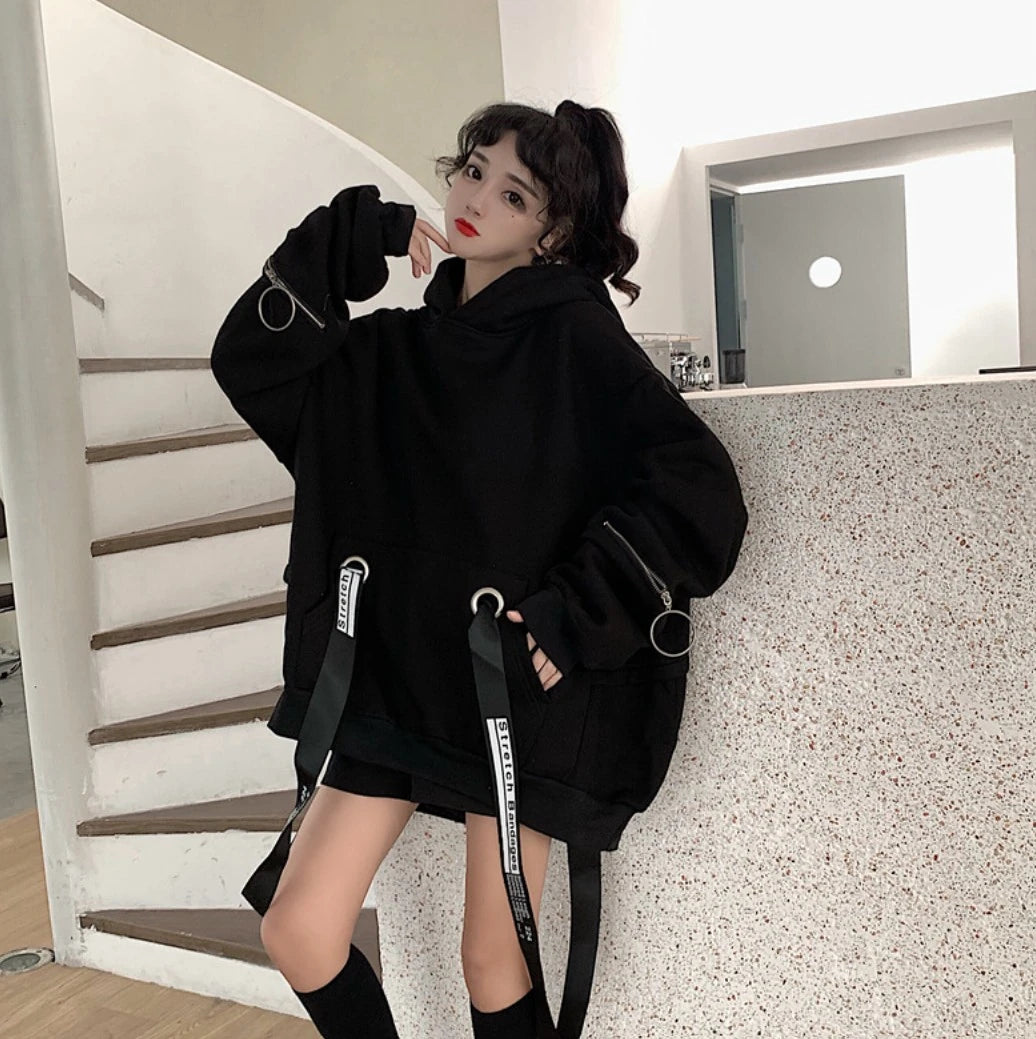 黒のオーバーサイズパーカーを着たモデル。螺旋階段のそばで立ち、片手を頬に添えるポーズ。