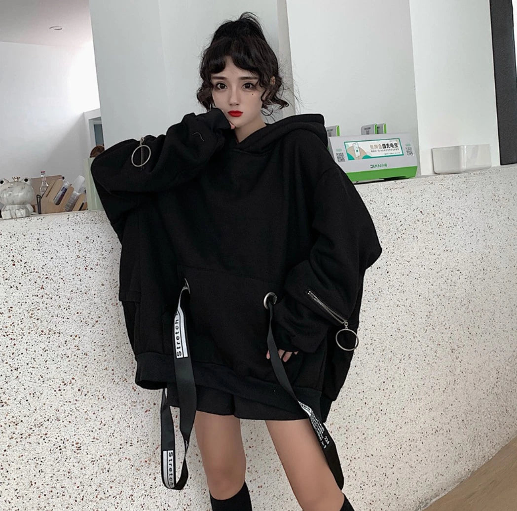 黒のオーバーサイズパーカーを着たモデル。正面立ち姿、片手を顎に添え、ストラップを強調。