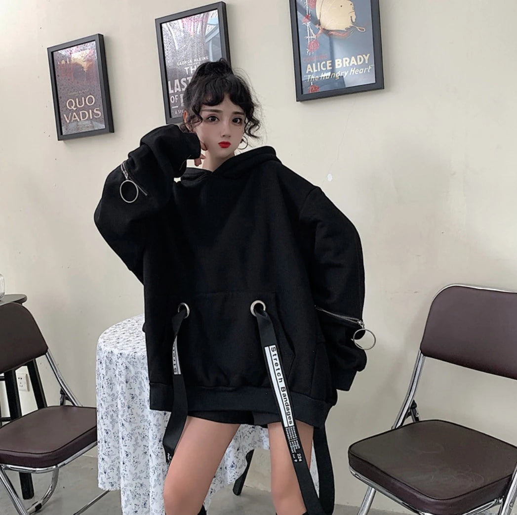 黒のオーバーサイズパーカーを着たモデル。少し首を傾げ、片手を顔に添えたポーズ。