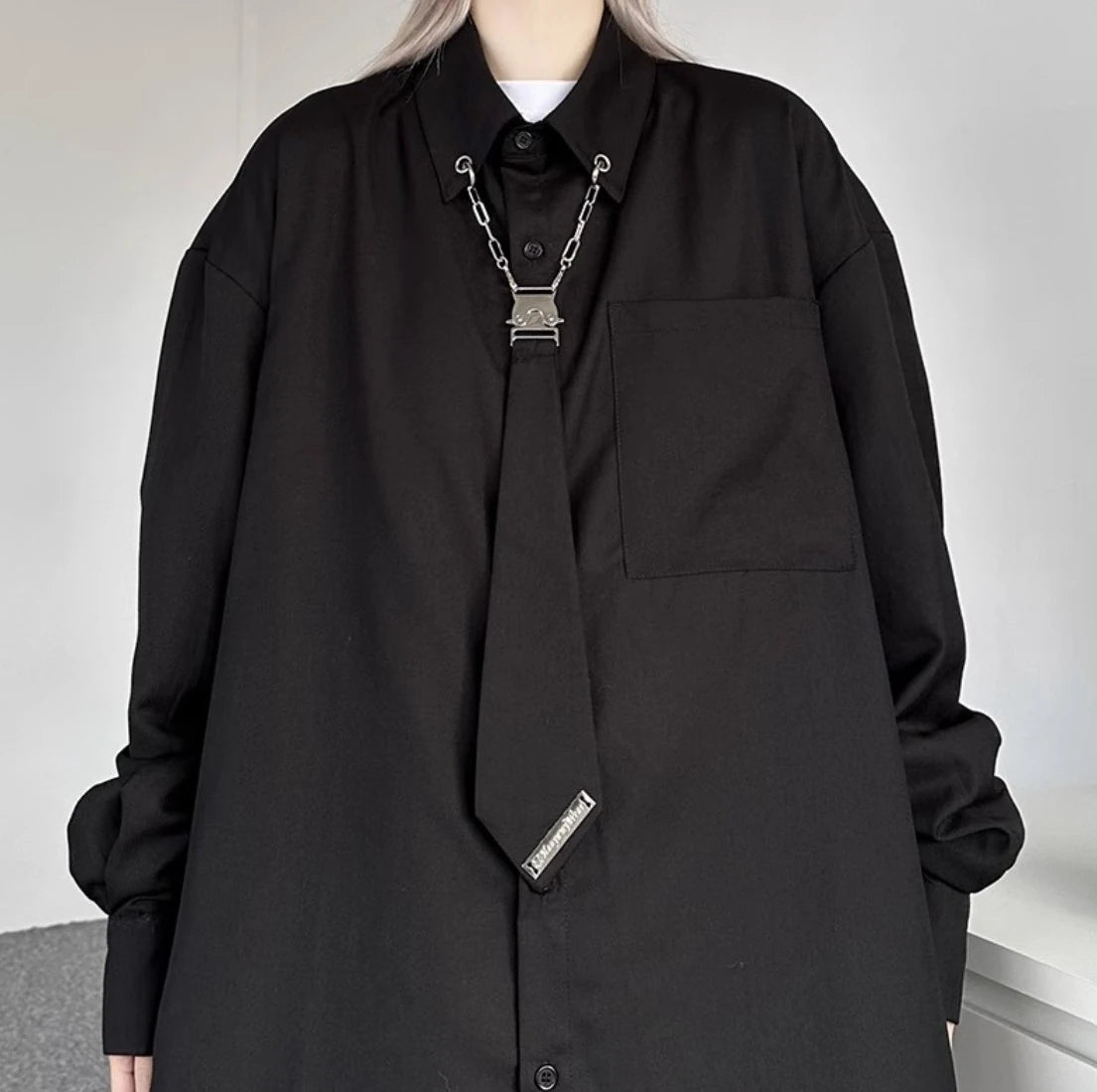 黒シャツの胸元クローズアップ。襟元のメタルチェーン、クリップ、そしてネクタイ風の装飾のディテール詳細。