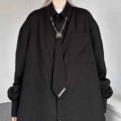 黒シャツの胸元クローズアップ。襟元のメタルチェーン、クリップ、そしてネクタイ風の装飾のディテール詳細。