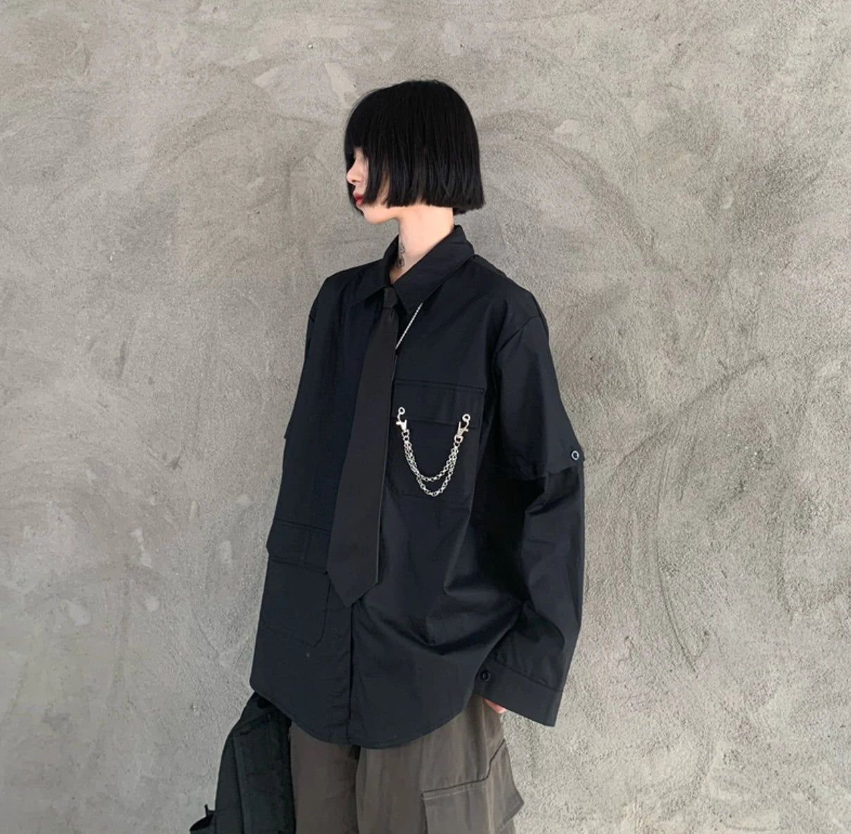 黒のネクタイ付きシャツを着たモデル。横向きの立ち姿。黒髪ボブヘア。