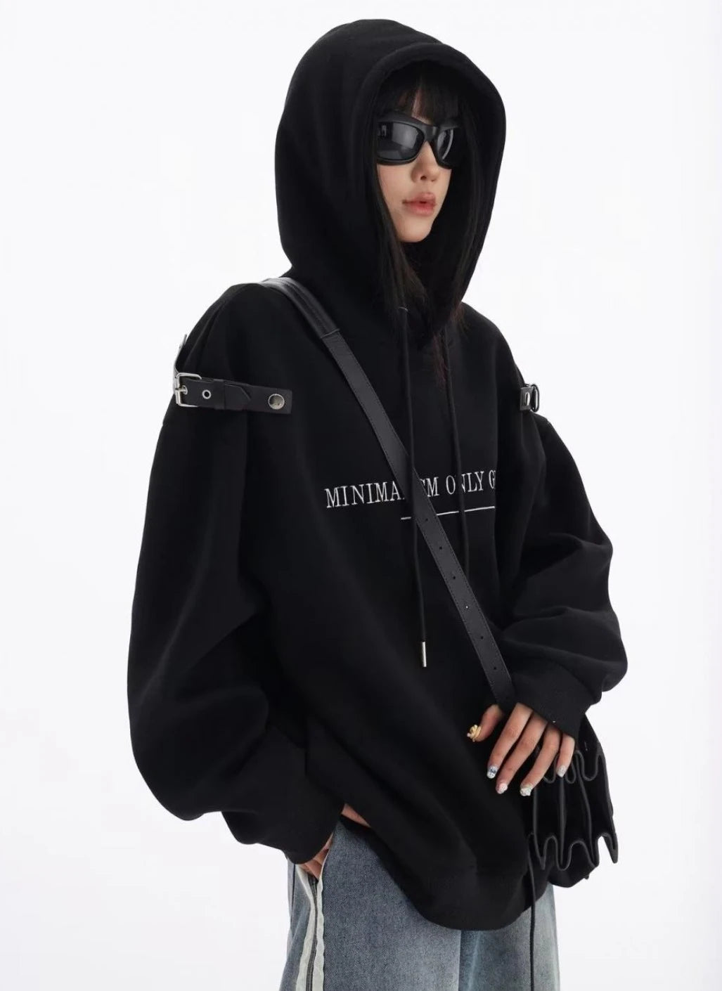 黒のショルダーベルト付きオーバーサイズパーカーにデニムパンツを合わせた上半身コーデ。フードをかぶったモードストリートスタイル。