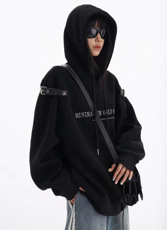 黒のショルダーベルト付きオーバーサイズパーカーにデニムパンツを合わせた上半身コーデ。フードをかぶったモードストリートスタイル。