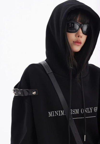 黒のショルダーベルト付きオーバーサイズパーカーのフードをかぶったアップカット。サングラスと胸元ロゴが際立つモードな表情。