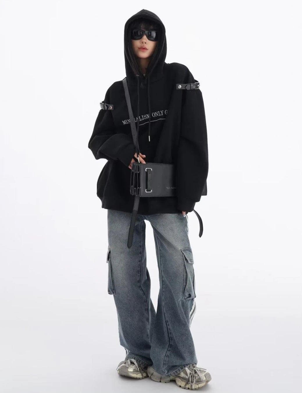 黒のショルダーベルト付きオーバーサイズパーカーにワイドカーゴデニムを合わせた全身コーデ。フロントバッグを斜め掛けしたモードストリートスタイル。