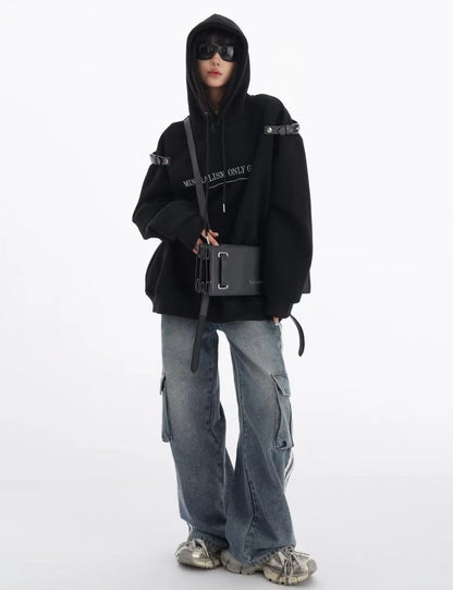 黒のショルダーベルト付きオーバーサイズパーカーにワイドカーゴデニムを合わせた全身コーデ。フロントバッグを斜め掛けしたモードストリートスタイル。