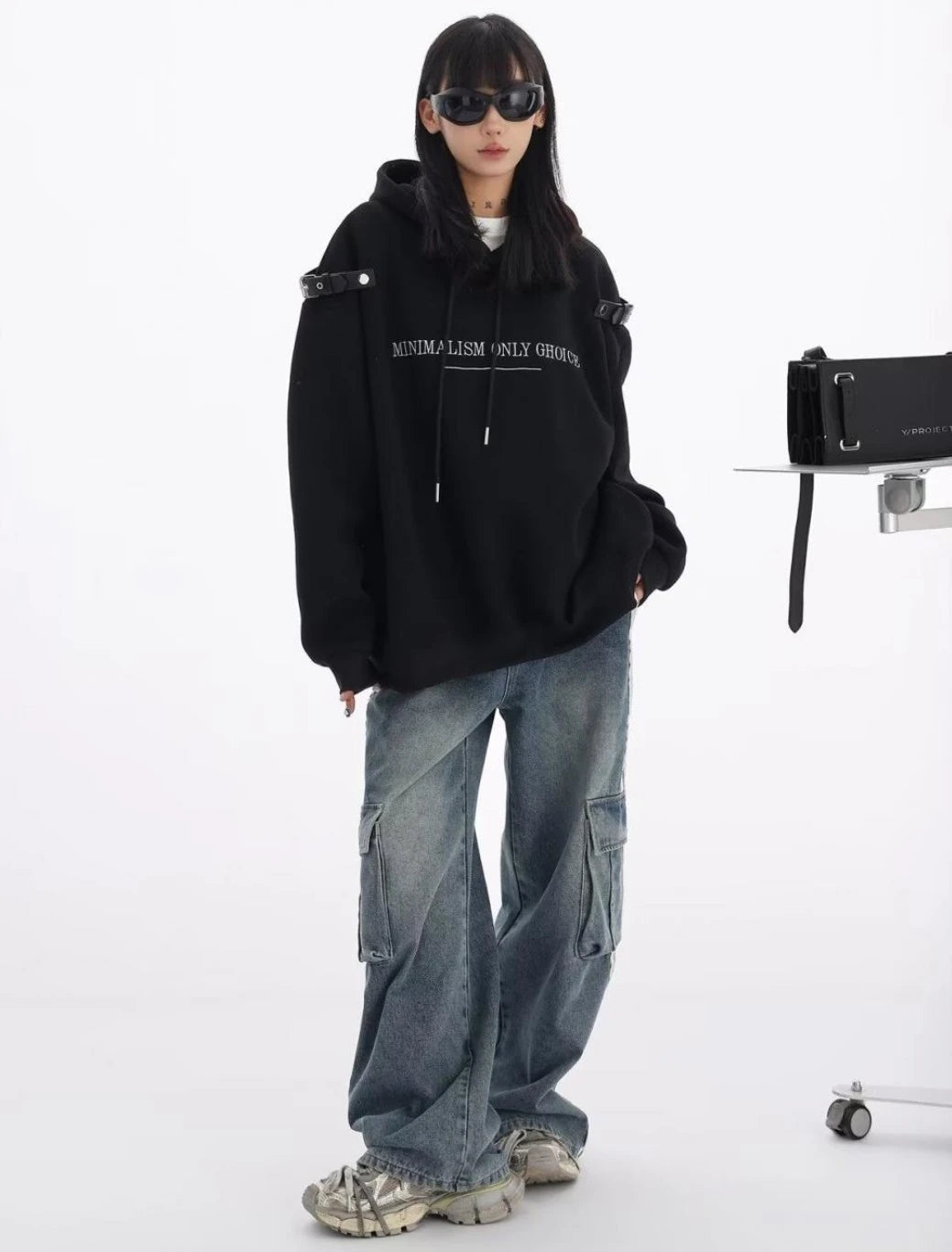 黒のショルダーベルト付きオーバーサイズパーカーとワイドカーゴデニムの全身コーデ。スニーカー合わせのカジュアルストリートスタイル。