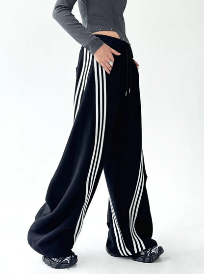 黒のスポーティーなワイドパンツを着用し、片腕を上げたダイナミックなポーズ。全身のシルエットを強調した一枚。