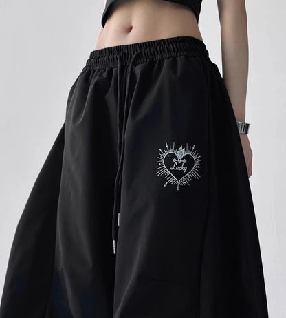 黒いストリート系パンツを着用し、両手をウエストに添えた全身写真。左太もものハート型「Lucky」刺繍ロゴが目立つ。