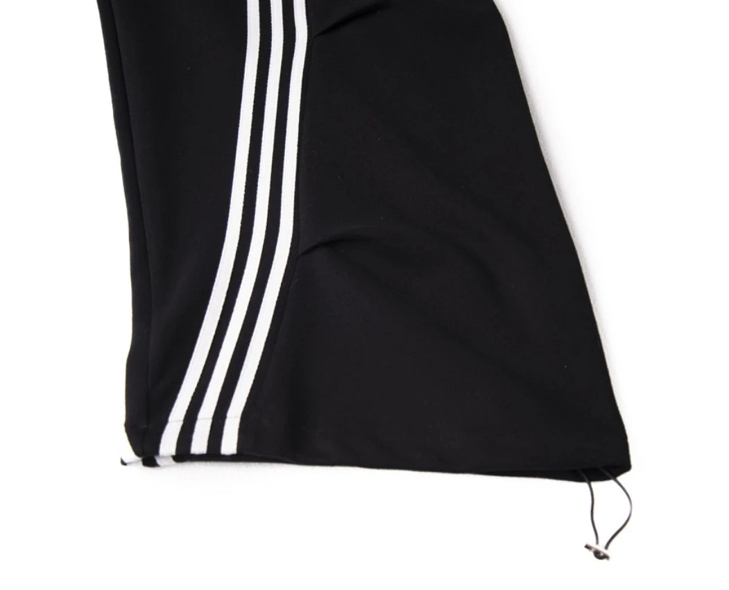 黒のワイドパンツを着用し座ったポーズ。太いラインがカーブを描くディテールと、裾のボリューム感。