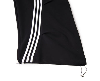 黒のワイドパンツを着用し座ったポーズ。太いラインがカーブを描くディテールと、裾のボリューム感。