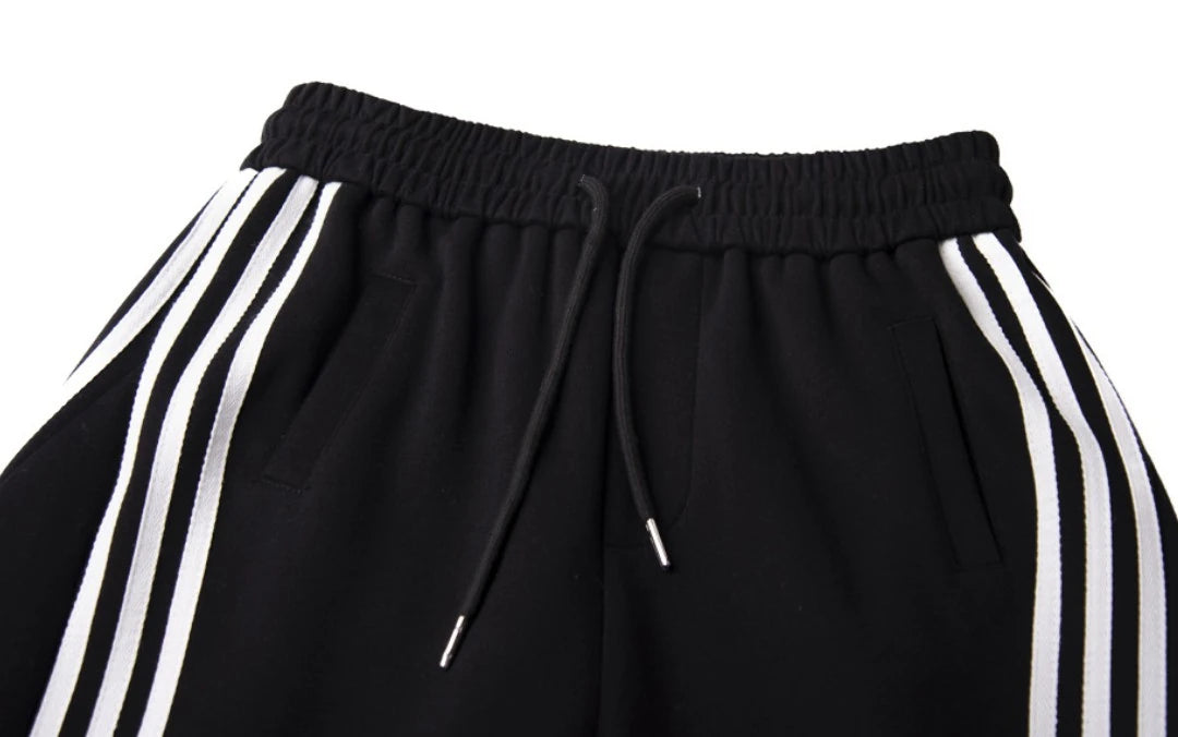 黒のワイドパンツのウエスト部分のクローズアップ。伸縮性のあるゴムウエスト、ドローコード、サイドの3本ラインのディテール。