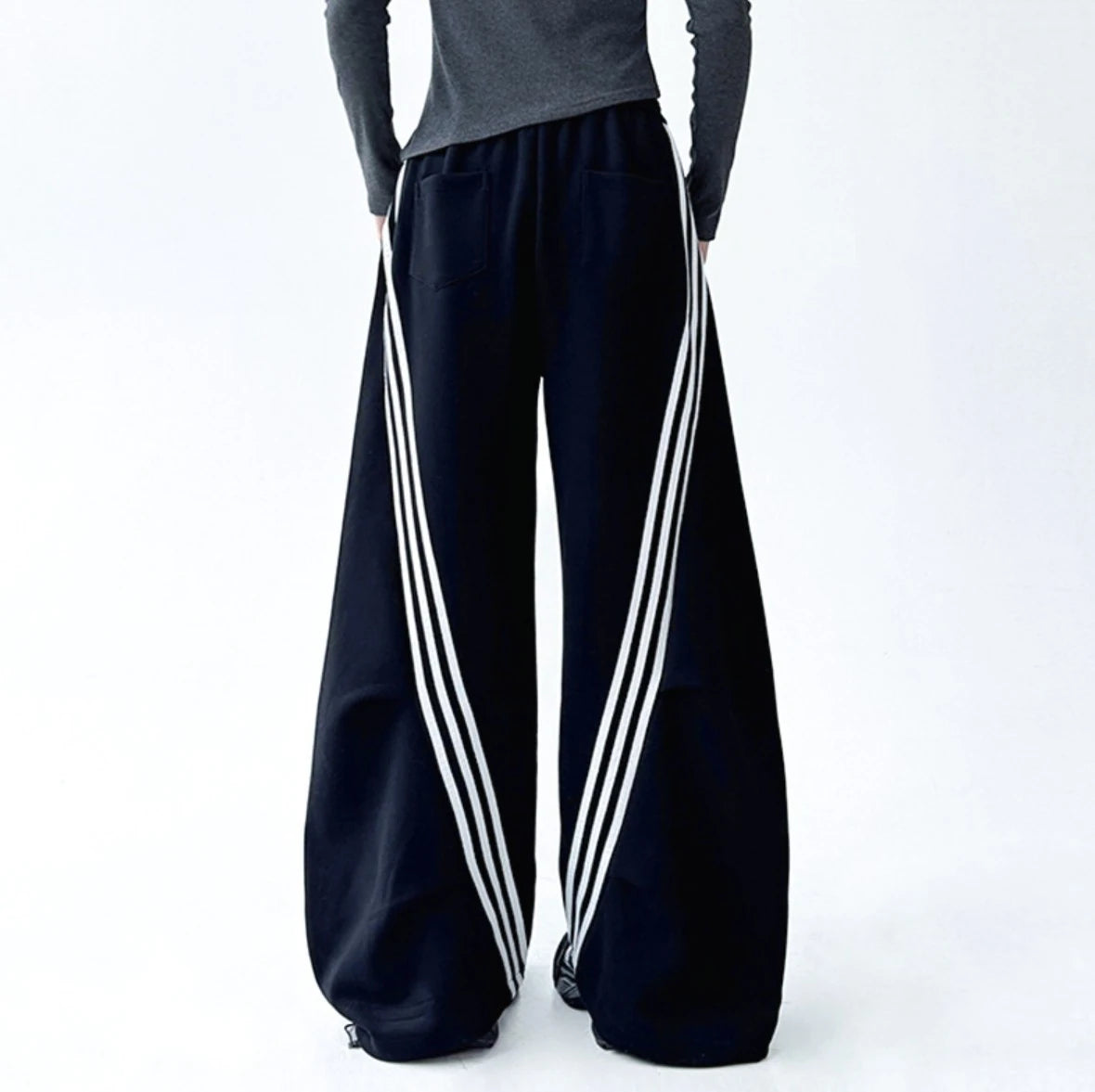 黒のワイドパンツを着用した後ろ姿。ヒップポケットのデザインと、サイドから見える白のラインがアクセント。