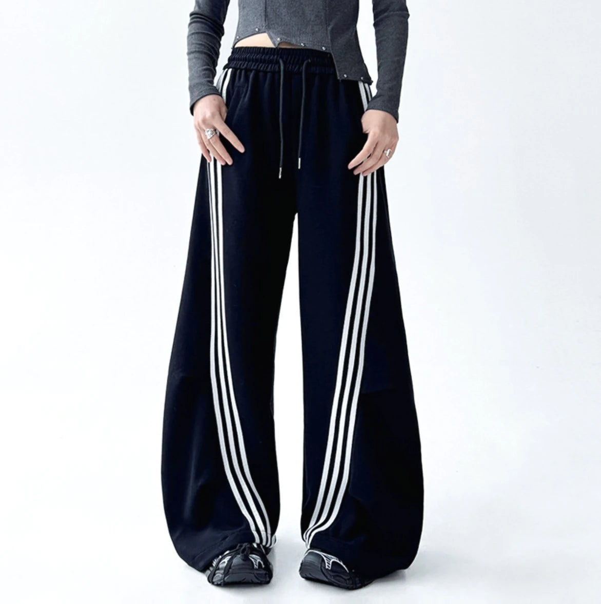 フロントに大きくカーブする3本ラインが特徴的な黒のワイドパンツ。ポケットに手を入れた正面の立ち姿。