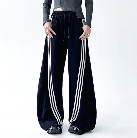 フロントに大きくカーブする3本ラインが特徴的な黒のワイドパンツ。ポケットに手を入れた正面の立ち姿。