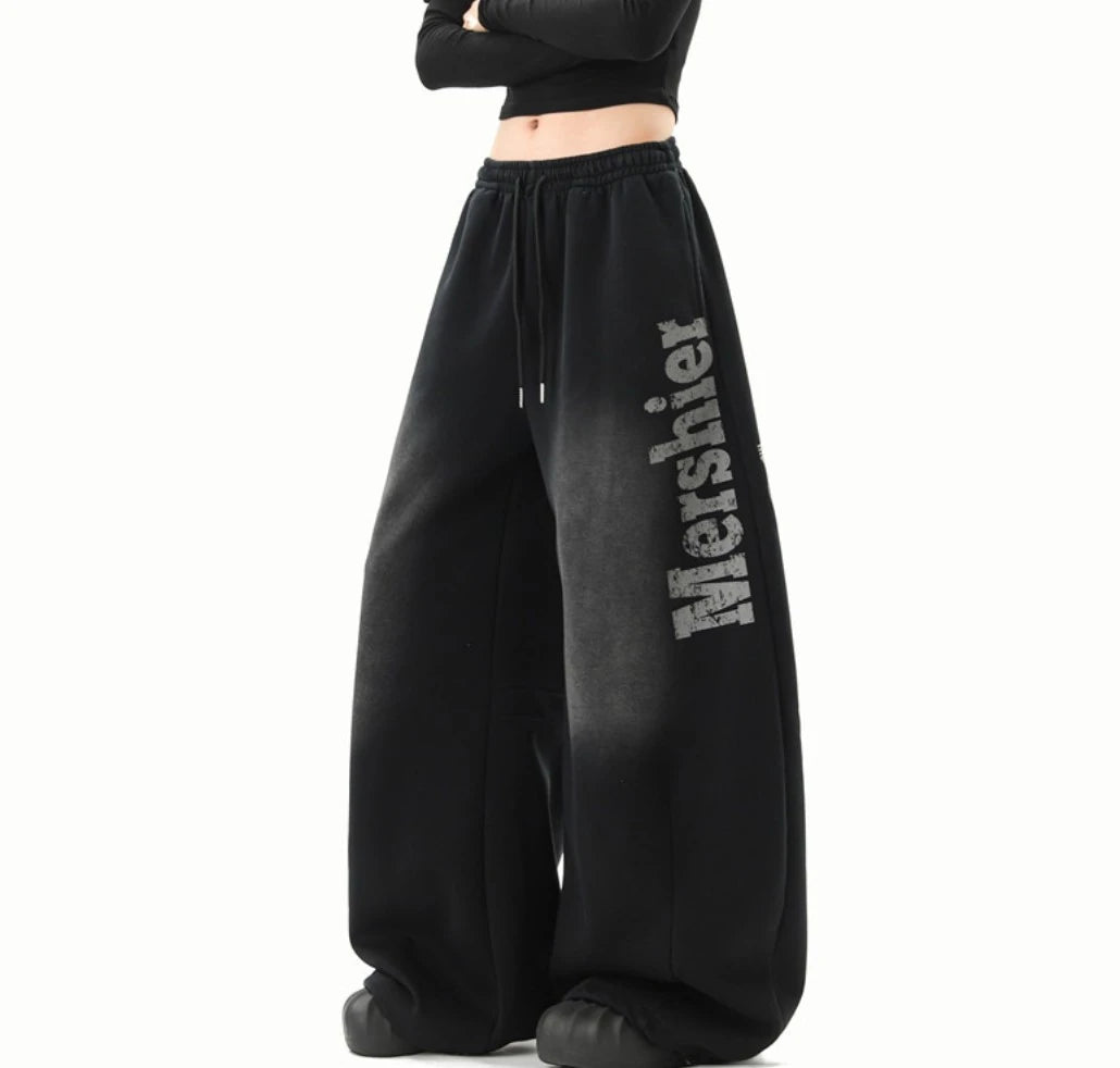黒のワイドスウェットパンツのサイドビュー。すっきりとした立ち姿で、色落ち加工と「Mershier」ロゴがよく見える。