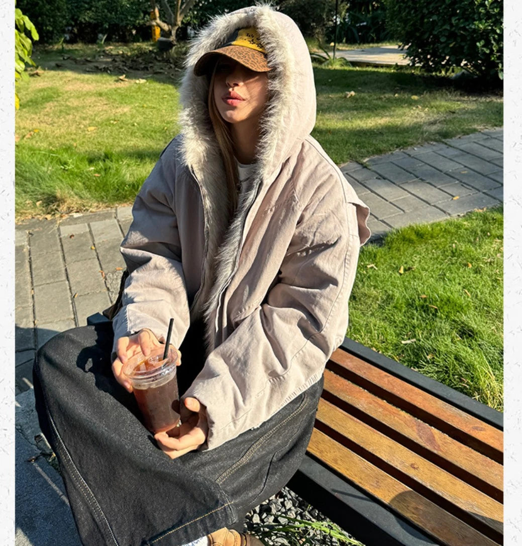 公園のベンチに座り、アイスコーヒーを持つ女性。ブルゾンのフードを被ったスタイル。