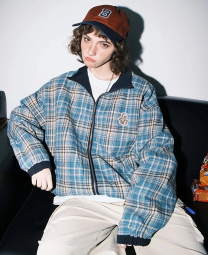 ブルーチェック柄側のリバーシブルジャケットを着たモデル。右手を膝に置いたポーズ。