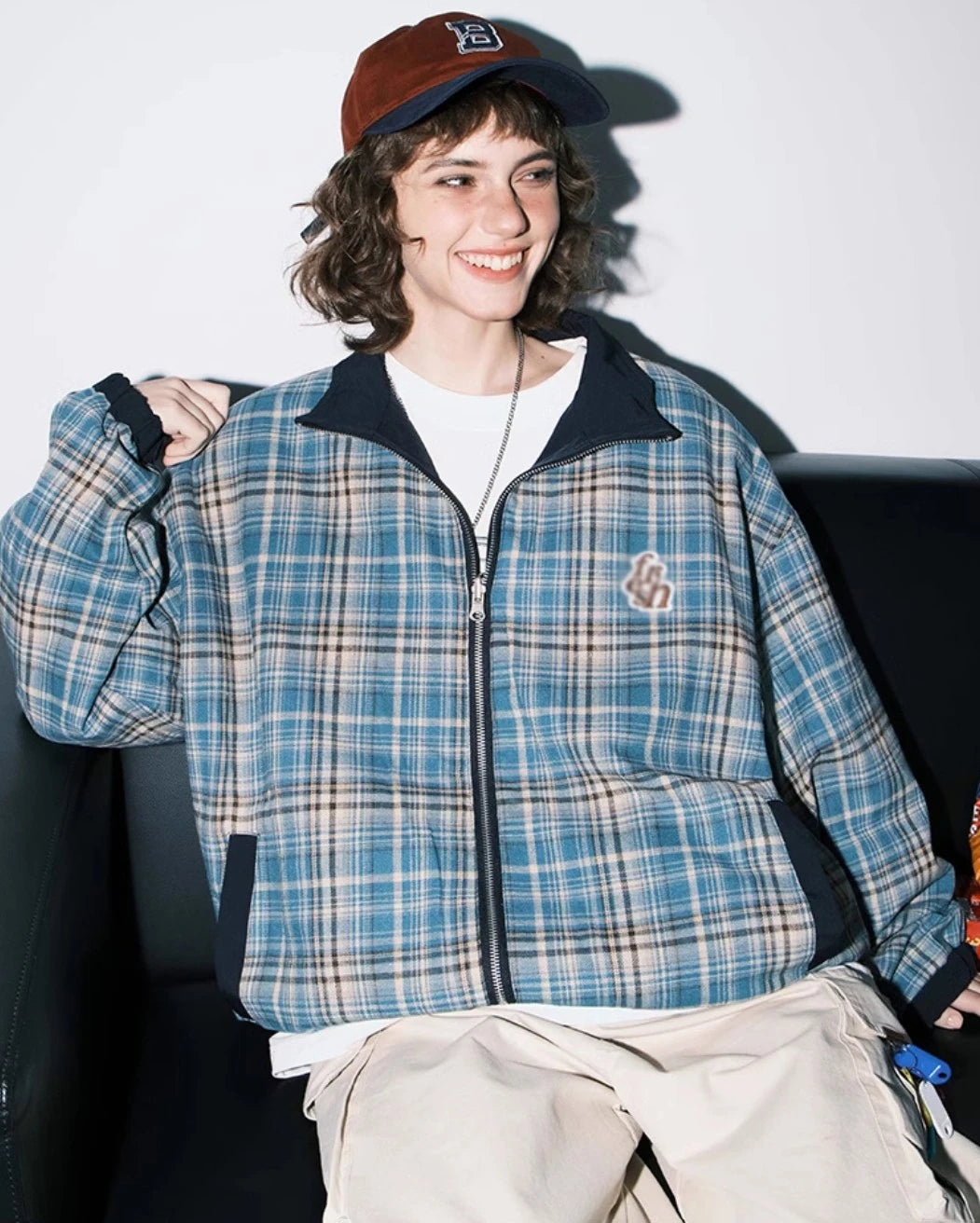 ブルーチェック柄側のリバーシブルジャケットを着たモデル。ソファで笑顔、リラックス。