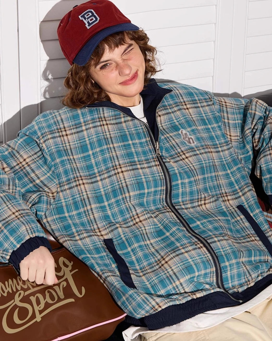 ブルーチェック柄側のリバーシブルジャケットを着たモデル。笑顔でウィンク、クローズアップ。