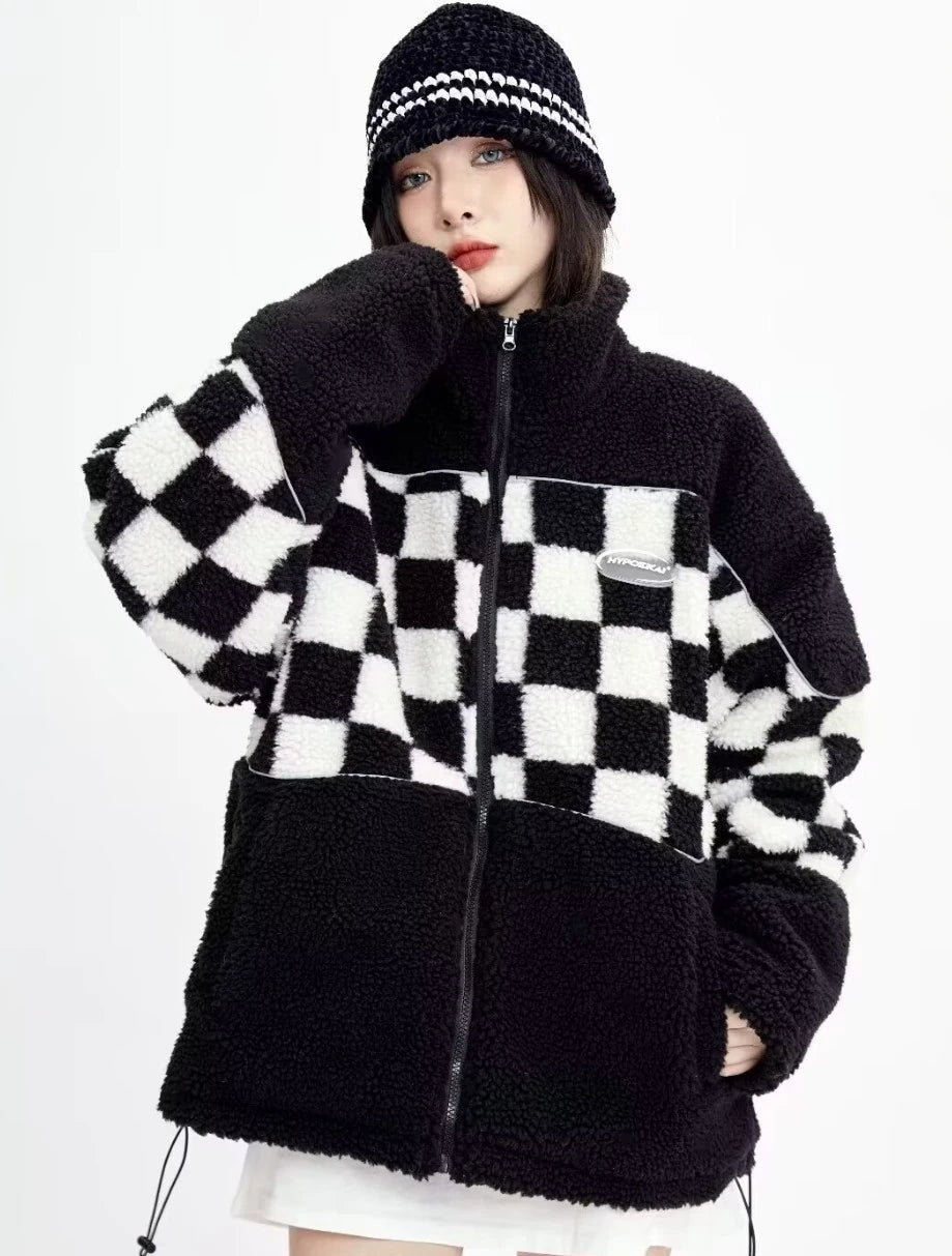 白黒チェックのボアジャケットを着用し、あごに手を添えたポーズ。ボリューム感のある袖と襟元のデザイン。